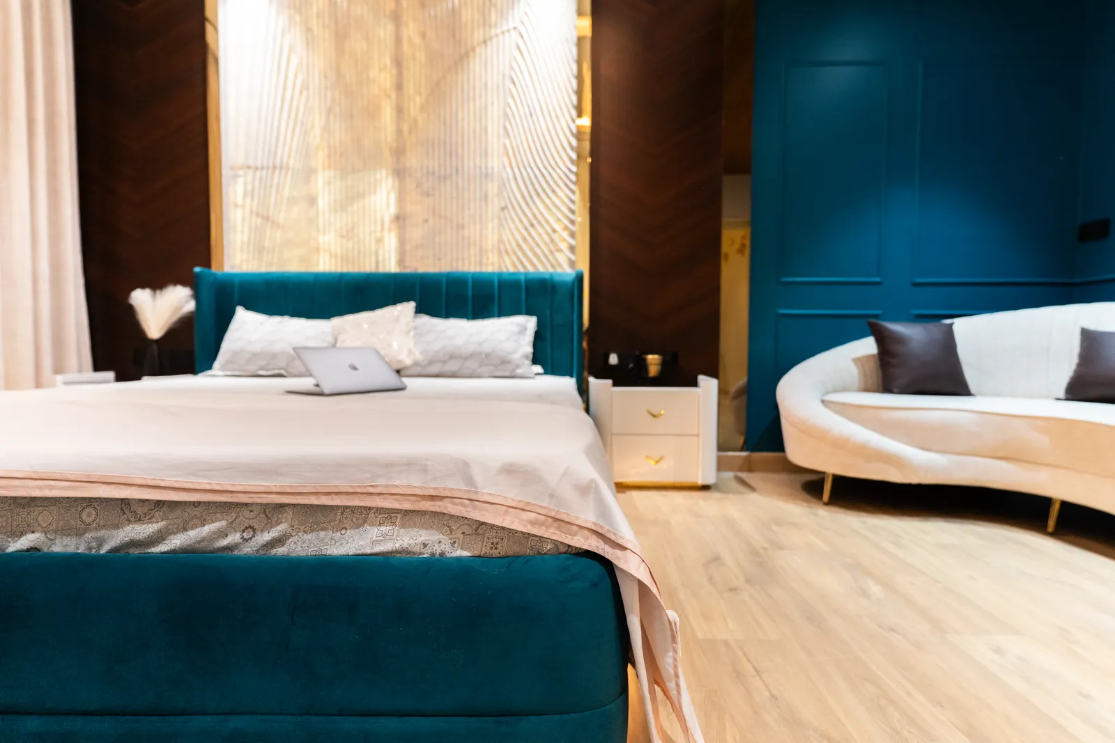 Bedroom with teal upholstered bed, curved cream sofa and backlit onyx panel — Abhishek's Residence